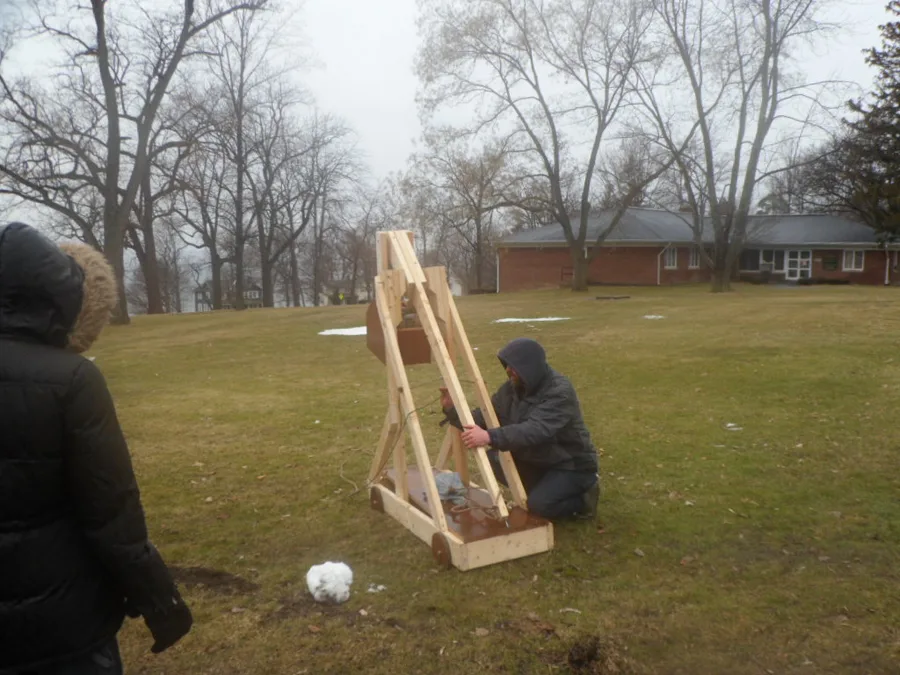Two students loading a wooden trebuchet they built, in the field behind the school.