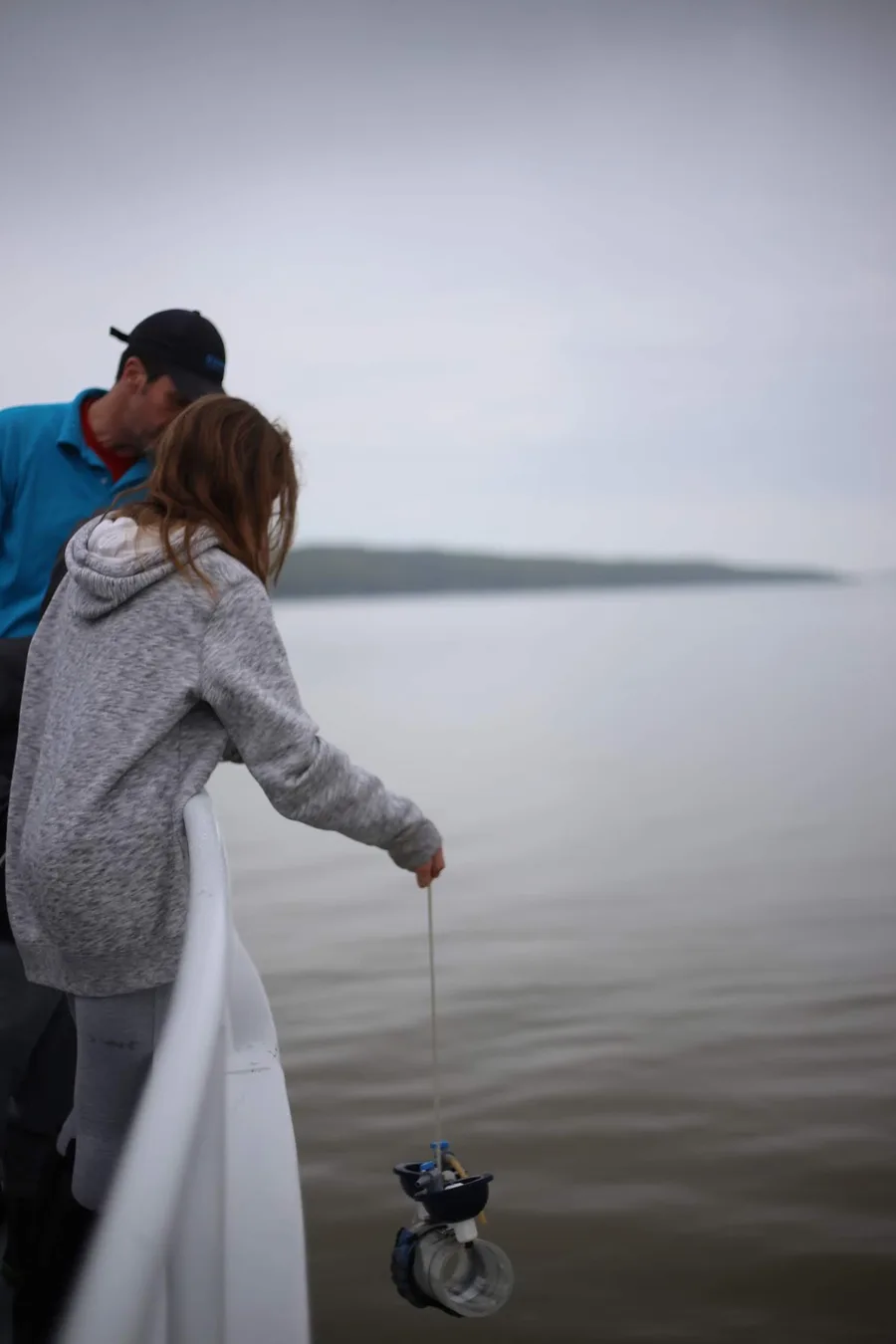 A student lowering a sampling line into Cayuga Lake from the shore.